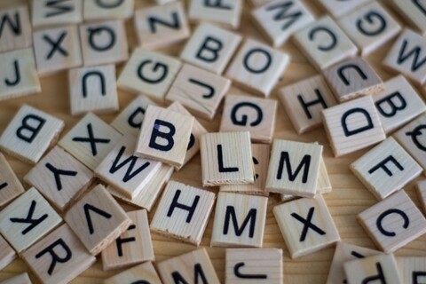 Quadratische Holzteilchen mit verschiedenen Buchstaben bedruckt auf einem Holztisch